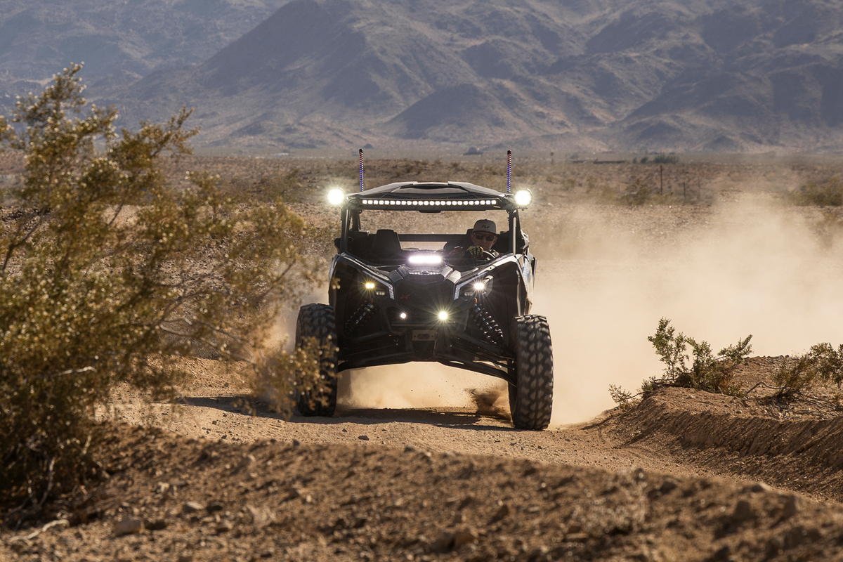 Can-Am Maverick X3 driving on a dusty desert trail with LED lights on