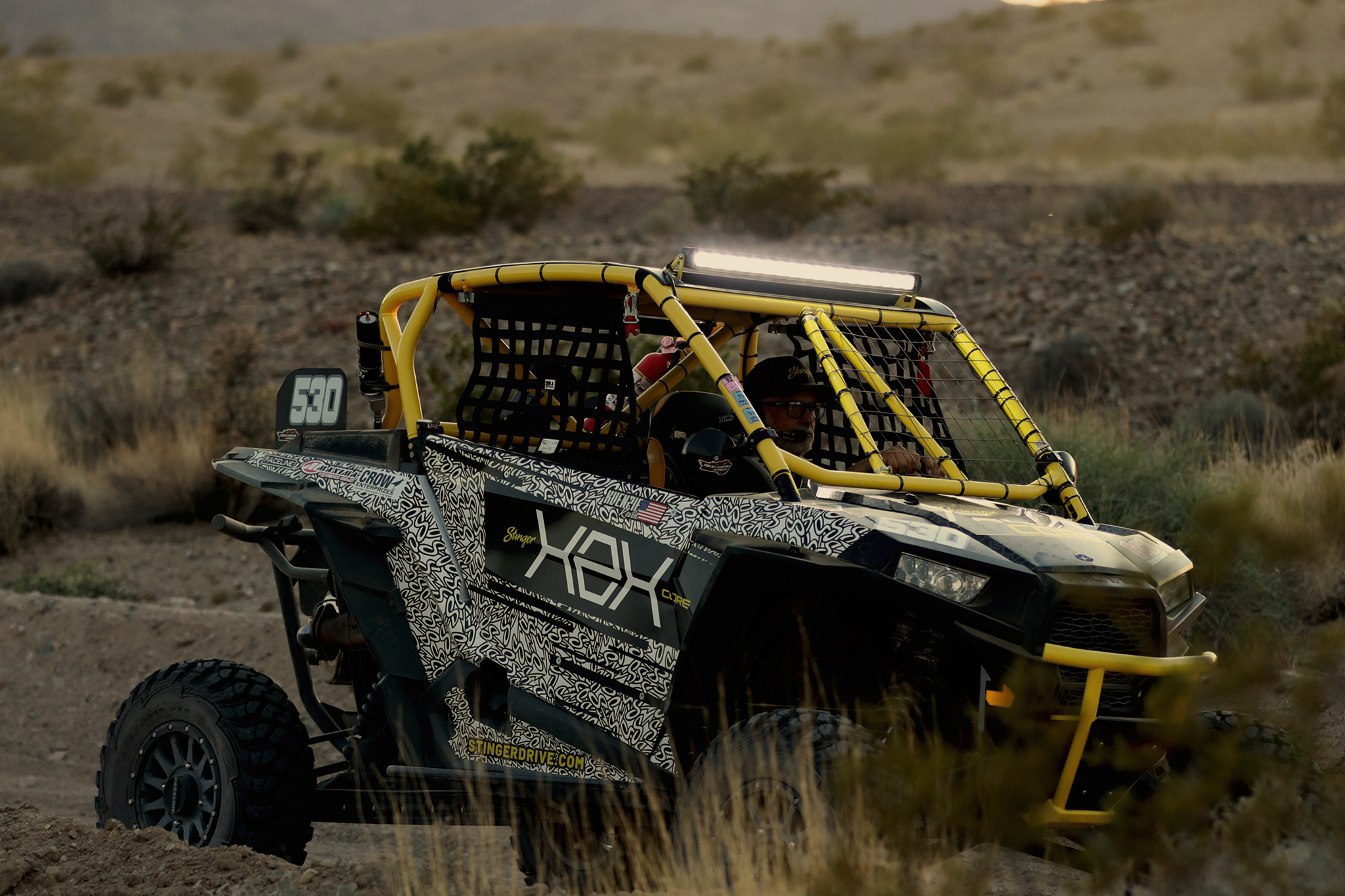 Stinger off road vehicle with yellow roll cage and patterned wrap driving through desert terrain