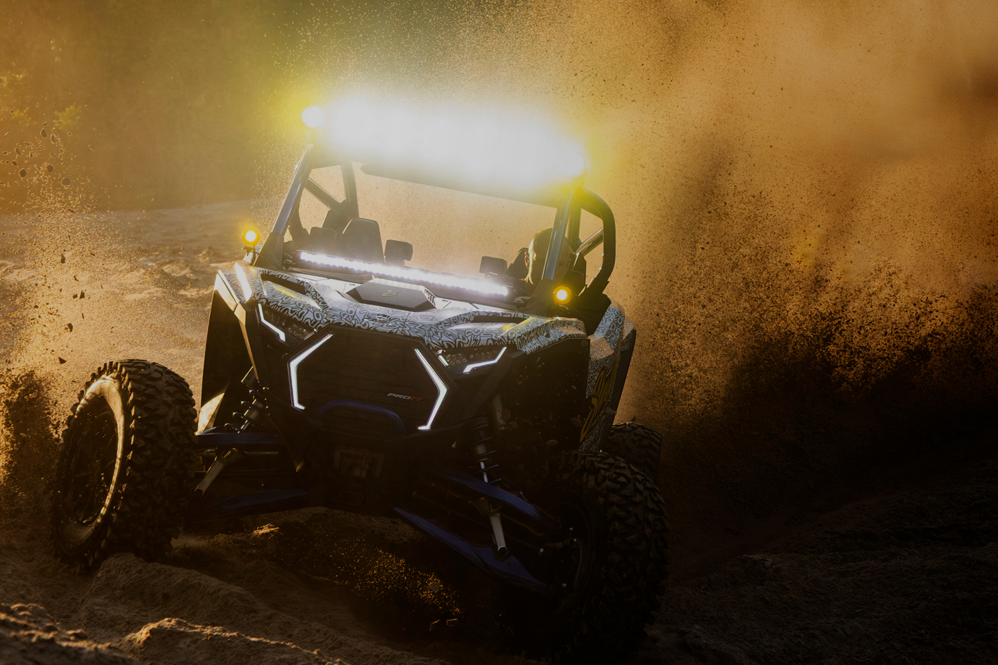 Polaris RZR Pro R off road vehicle driving through dirt with bright LED light bar illuminated