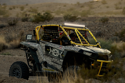 Stinger off road vehicle with yellow roll cage and patterned wrap driving through desert terrain
