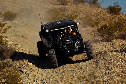 Black off-road vehicle driving on a dirt trail in a desert landscape